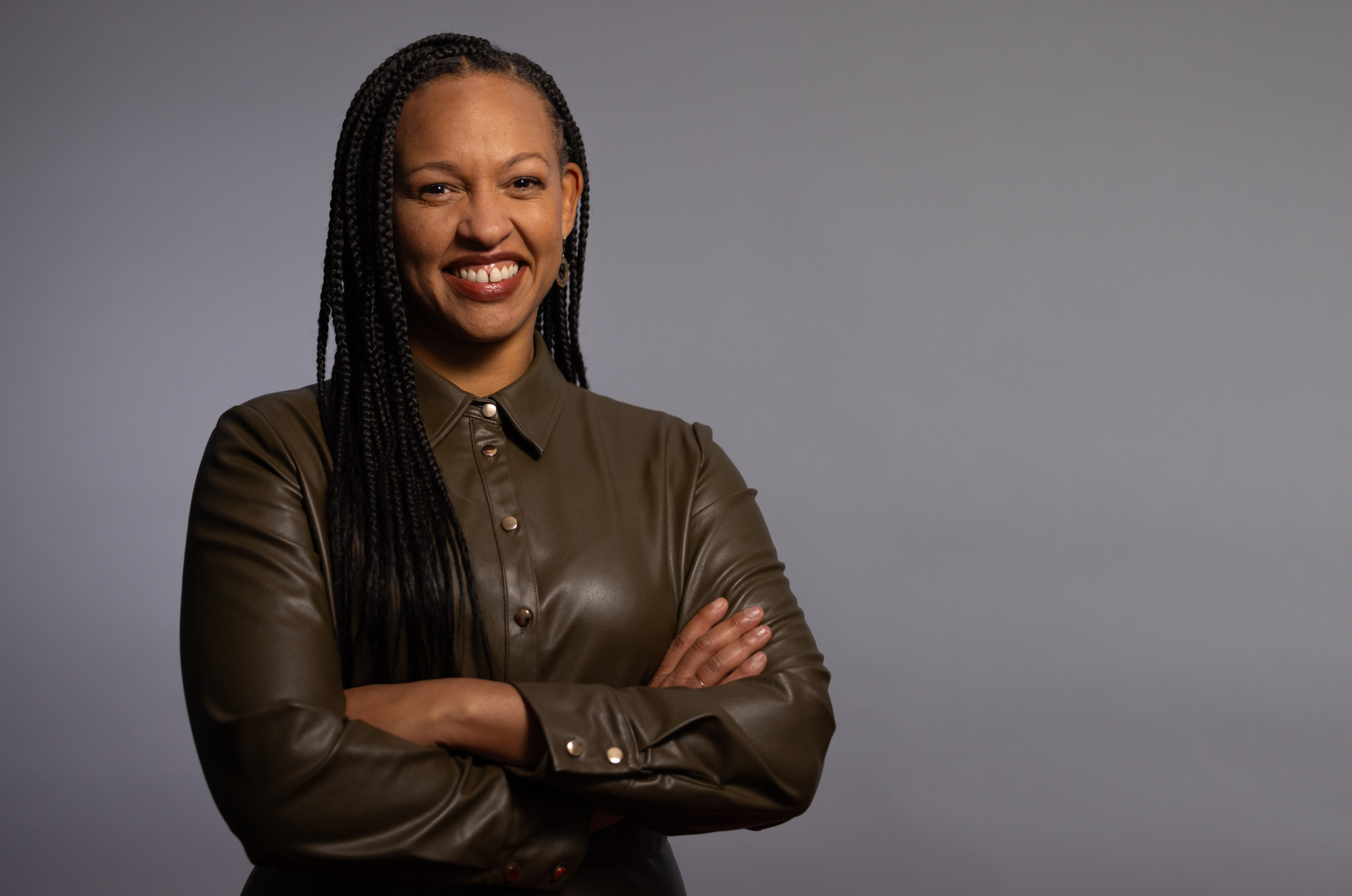 Woman smiling with her arms crossed in front of a grey backdrop 